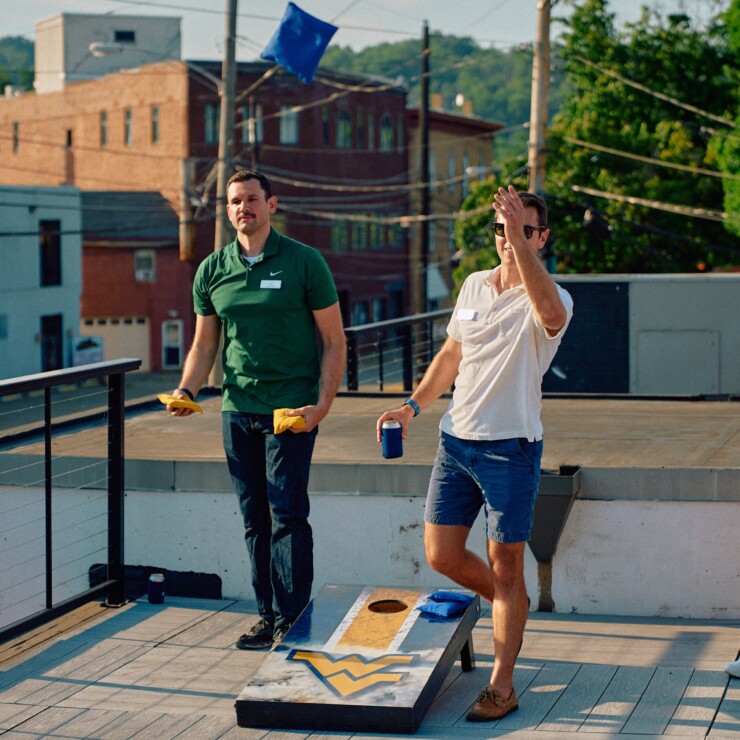 Two men playing cornhole on a summer rooftop.