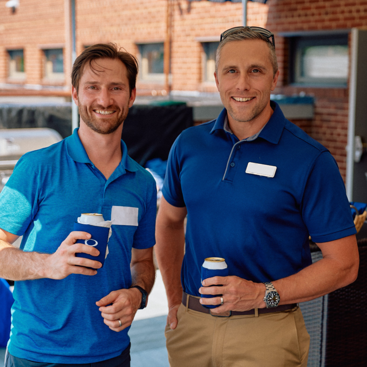 Two men smiling with drinks in hand.