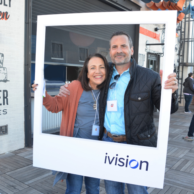Two people holding up a picture frame ivision cutout.